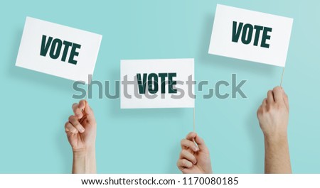 Hands raise the white flags with the word VOTE up. The concept of voting, making choices. Presidential and parliamentary elections. Calling for voting, democracy.