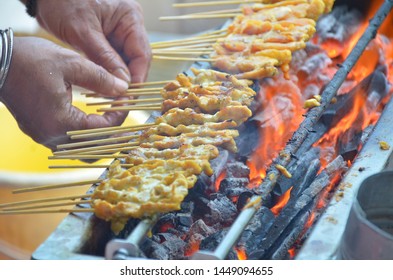 Hands roasting pork satay on barbecue grill with flames. Thai street food, seasoned meat or chicken skewered with bamboo stick