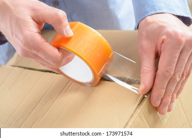 Hands With Roll Of Transparent Packaging, Adhesive Tape On A Cardbox