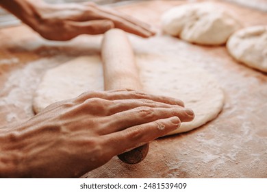 Hands rolling dough with a wooden rolling pin on a floured surface, making homemade bread or pizza - Powered by Shutterstock