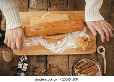 Hands rolling gingerbread dough with wooden rolling pin for christmas traditional cookies. Making christmas gingerbread cookies on rustic table with metal cutters, spices, decorations. Top view