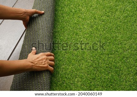 Hands rolling a green imitation grass. The material is for carpet, flooring, wall and sports stadiums.  Good for indoor and outdoor usage.  Durability, decoration, objects, background and textures.