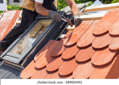 Hands of roofer laying tile on the roof. Installing natural red tile using hammer