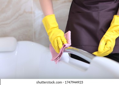 Hands in rubber gloves wipe chrome surfaces in the bathroom. The concept of cleanliness and hygiene in a hotel or home. Unrecognizable photo.