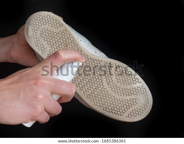 Hands sanitizes\
shoe sole against coronavirus. Disinfectant spray on the sole of\
shoe isolated on black\
background