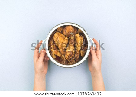Hands with a saucepan filled with fried roasted chicken, top view, kitchen workspace background, top view 