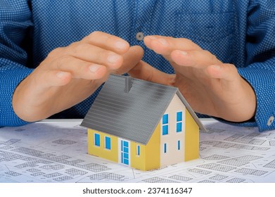 Hands saving small moled house with an imaginary cadastral map - Protect your house concept