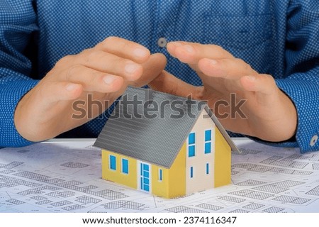 Hands saving small moled house with an imaginary cadastral map - Protect your house concept