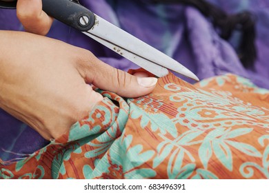 Hands with scissors cutting a piece of textiles