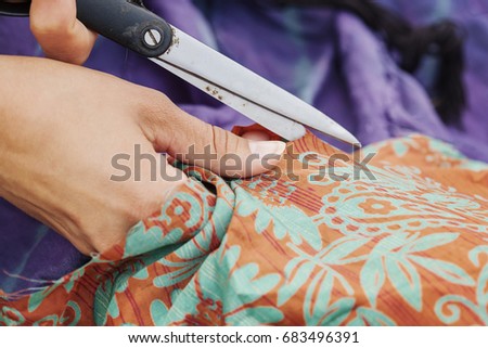 Hands with scissors cutting a piece of textiles