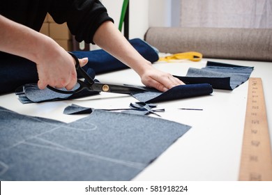 Hands of seamstress cutting a jeans fabric with scissors on white table 