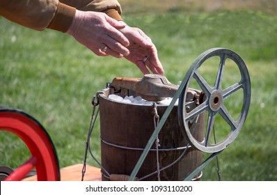 Hands Are Seen Adding Ice To An Old Fashioned Ice Cream Maker That Is Pulley And Gas Driven To Mix Up The Dessert