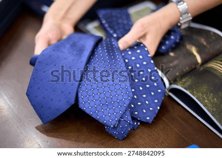 Hands selecting blue patterned neckties from magazine spread on wooden table, menswear fashion.