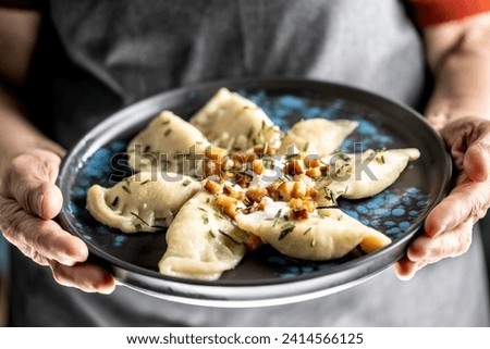 The hands of a senior home cook hold a plate with a national Slovak dish - Bryndzove Pirohy.