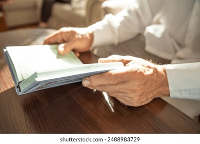 Hands of senior man holding Quran at home. Natural aesthetic light. Pages with the text of Surah in Arabic. - Powered by Shutterstock