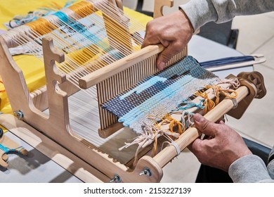 Hands of senior man weaving small rug with pattern on manual table loom, at masterclass on weaving. Handmade concept