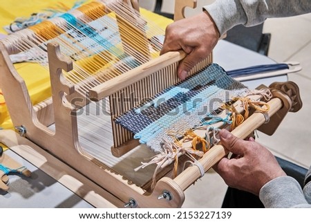 Hands of senior man weaving small rug with pattern on manual table loom, at masterclass on weaving. Handmade concept Photo stock © 