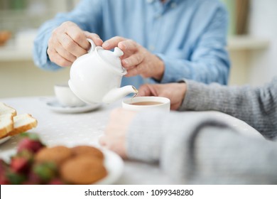 Hands of senior man with white china teapot pouring tea into cup of his wife - Powered by Shutterstock