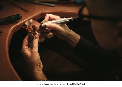 Hands of senior woman goldsmith polishing off the sharp edges on a ring at her workbench. Jewelry designer making ring surface seamless with polishing machine.