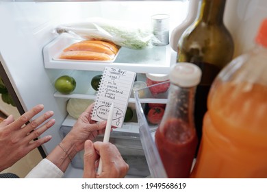 Hands Of Senior Woman And Her Adult Son Writing Shopping List When Checking Fridge