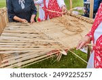 Hands of senior women weave bast cloth on wooden loom at Siberian Tatar festival. Bast weaving is ancient craft.