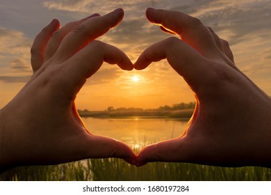 Hands in the shape of heart against the sunset over the lake or river in the summer with a cloudy sky background. Landscape. - Shutterstock ID 1680197284