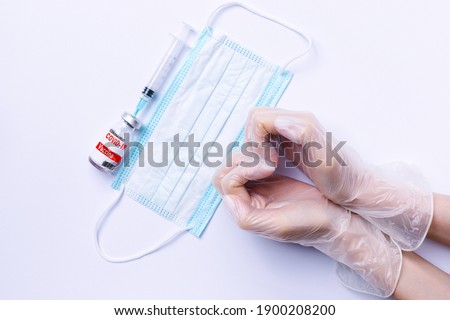 Hands in the shape of a heart in gloves, covid 19 vaccine and a medical mask on a white background.