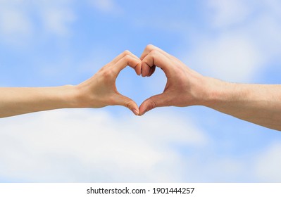 Hands in shape of love heart. Heart from hands on a sky background. Love, friendship concept. Girl and male hand in heart form love blue sky. Female and man hands in the form of heart against the sky.