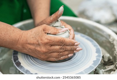 Hands shaping a clay vessel on a pottery wheel, surrounded by a messy workspace. The focus is on the craft and precision, highlighting the art of pottery making in a serene, creative environment. - Powered by Shutterstock