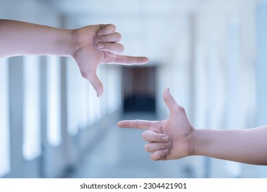 Hands show a crop gesture on the background of a blurred corridor.