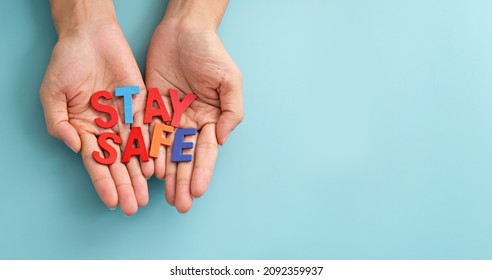 Hands showing multicolor wooden alphabet words "stay safe" on blue background. Stay Safe Message on Palm of Hand.