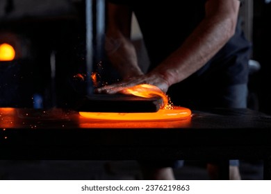 Hands of skillful unrecognizable male worker in black casual clothes cutting hot orange glass at table in factory - Powered by Shutterstock