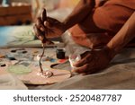 Hands skillfully holding palette knife and mixing paints on canvas. Background reveals artistic studio ambience with various art supplies and tools