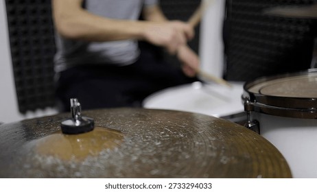 Drummer’s hands skillfully playing a drum set with drumsticks, creating dynamic rhythmic sound during a musical session, focusing on the cymbal and drum in a studio environment