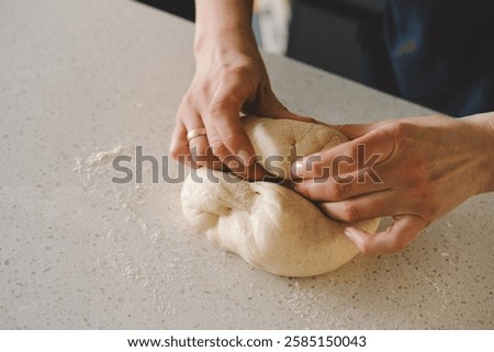 Hands are skillfully rolling and shaping dough on a clean kitchen countertop sprinkled with flour, healthy sourdough bread. The bright space suggests a cozy baking atmosphere.