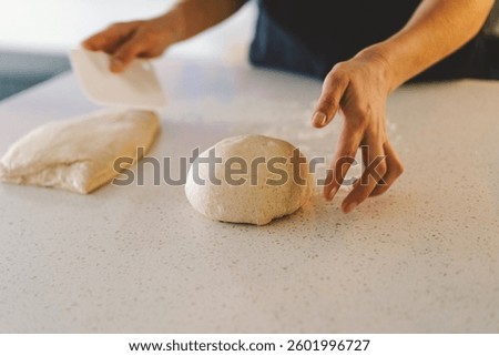Hands are skillfully rolling and shaping dough on a clean kitchen countertop sprinkled with flour, healthy sourdough bread. The bright space suggests a cozy baking atmosphere.