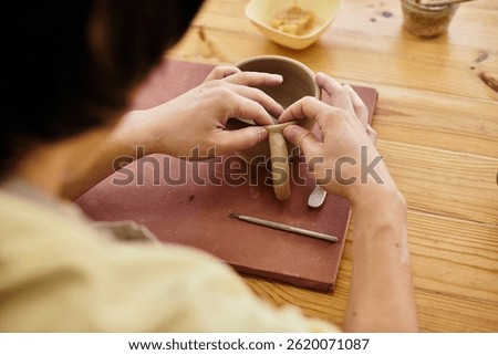 Hands skillfully shape clay into a distinctive mug within a well lit pottery studio.