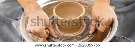 Hands skillfully shape wet clay into an elegant pot, surrounded by creative tools and art.