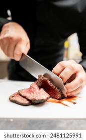 A chef’s hands skillfully slice a medium-rare steak with a large knife on a white plate