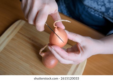 Hands skillfully slice through shallots on a wooden board in a cozy kitchen.
