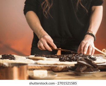 Hands skillfully spread chocolate and nut filling on dough, preparing traditional cozonac, a cherished Romanian bread made for holidays and celebrations
