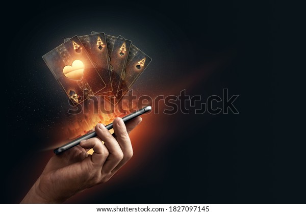 In the hands of a smartphone with playing cards,\
black-gold background. Concept of online gambling, online casino.\
Copy space