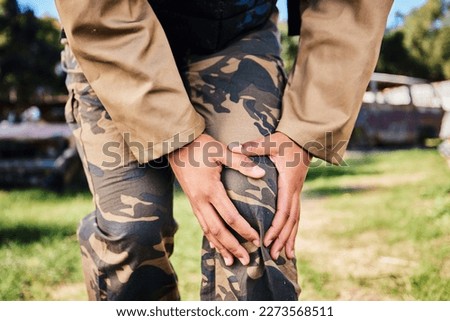 Hands, soldier and knee injury in paintball sport, running or military training from intense battle or war on grass field. Hand of sports army player holding painful leg ache, accident or bone