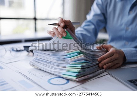Hands sorting a large stack of business documents, reports and files on a busy office desk, using colorful paper clips and binders for organized financial and administrative work