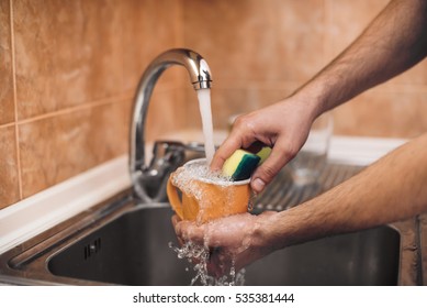 Hands with sponge wash the cup under running water