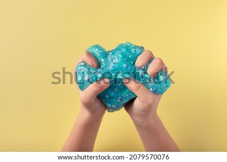 hands squeeze blue slime on yellow background. Antistress toy for kids. closeup. copy space