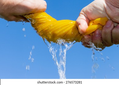 Hands squeeze wet yellow cloth against blue sky.