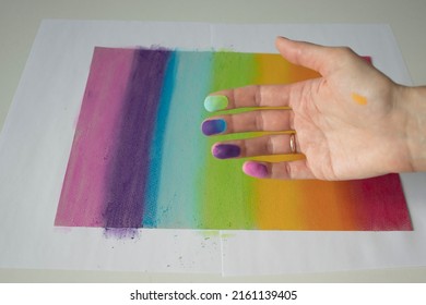 Hands stained with pastel crayons. A woman artist paints a picture of the colors of the rainbow.