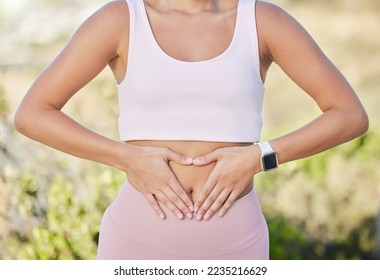 Hands, stomach and fitness of woman with diet, lose weight and wellness goals in park, nature and outdoor healing, training or yoga. Exercise, workout and gut health of girl with digestion hand sign