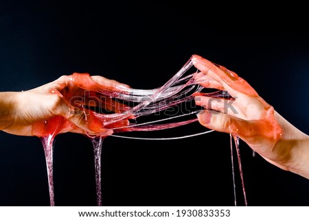 Hands stretch the slime poured on them on a black background